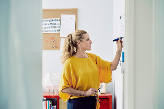 Woman writes ideas on a whiteboard in her London home office