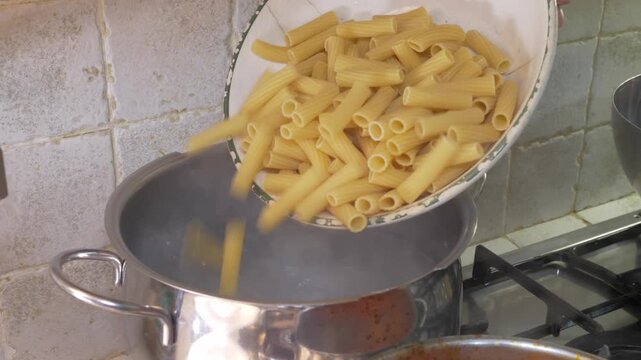 A woman's hand drops a generous portion of pasta into a pot of boiling water, the satisfying start of a classic Italian cooking ritual enjoyed in home kitchens across the country.