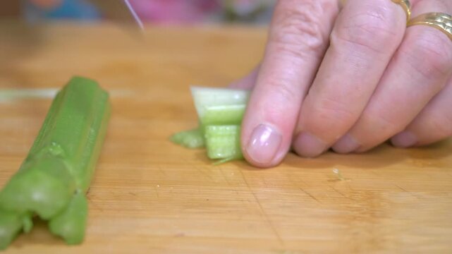 A knife slices cleanly through fresh celery stalks on a wooden cutting board, preparing the first element of the classic Italian soffritto base for a rich homemade pasta sauce.