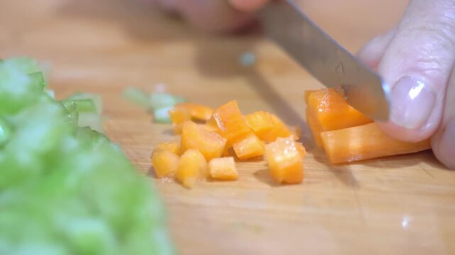 A knife slices cleanly through a fresh carrot on a wooden cutting board, preparing the sweet and colorful element of the classic Italian soffritto base for a homemade pasta sauce.