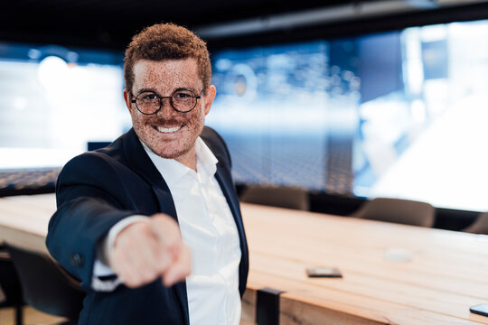 A smiling businessman points at the camera in a modern studio