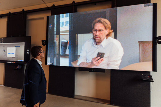 Businessman in office watches large screen during video call