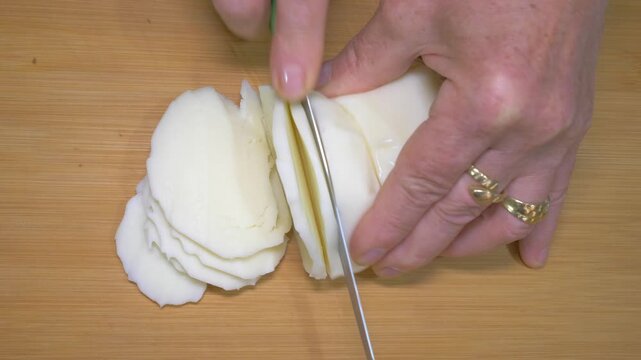 As the knife cuts through fresh scamorza cheese, its soft milky interior is revealed, showcasing the creamy texture that makes it an essential ingredient in southern Italian baked pasta.