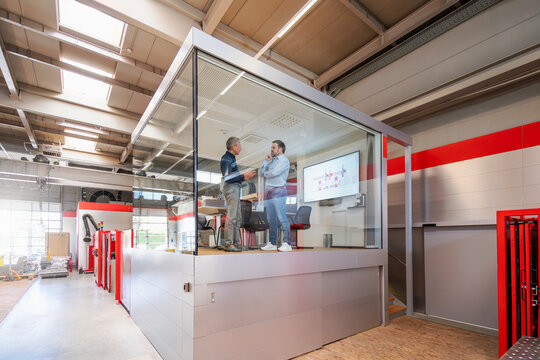 Male engineers discuss production inside a glass factory office