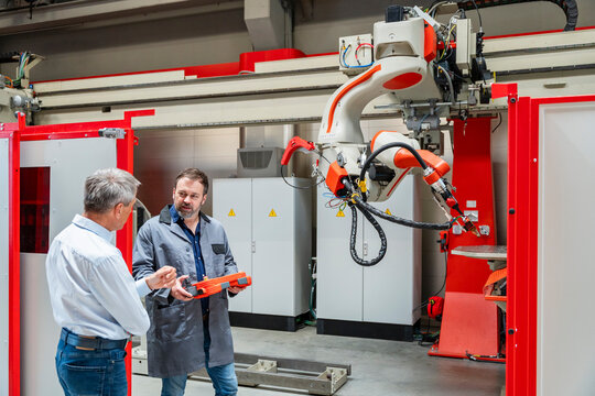 A manager and an engineer inspect an industrial robot at the factory