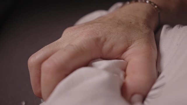 Close-up of a hand softly gripping a white bedsheet, conveying intimacy, comfort, vulnerability, and emotional connection. Suitable for wellness, romance, and cinematic storytelling.