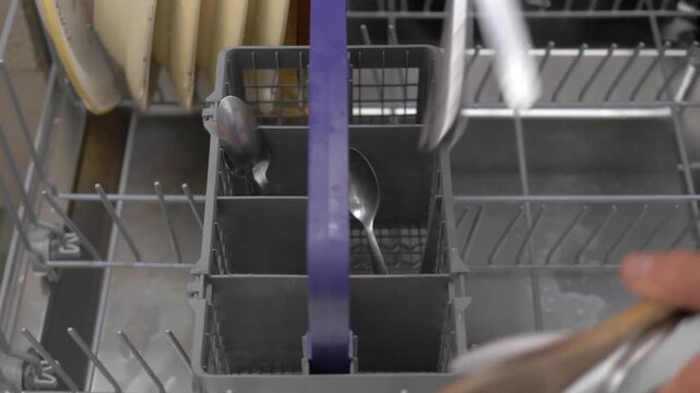 Vertical: A housewife methodically loads freshly rinsed dishes into the dishwasher, arranging each piece with care to ensure maximum cleaning efficiency during the wash cycle.