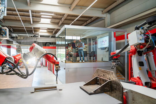 Men discuss business in a glass office inside a robot factory