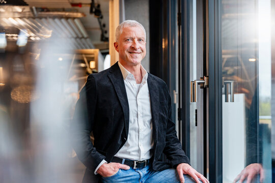 Smiling businessman leans against a window in a modern office