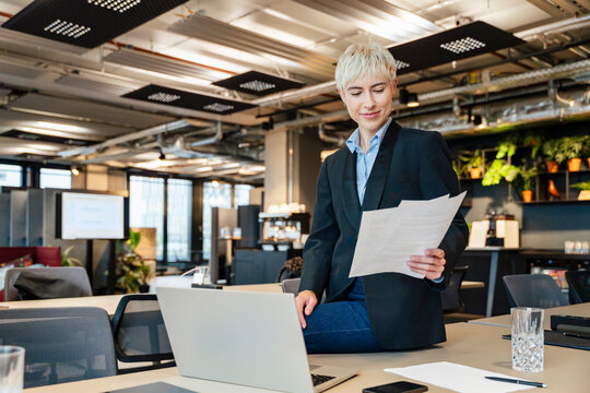 Smiling businesswoman reads document on desk in modern office