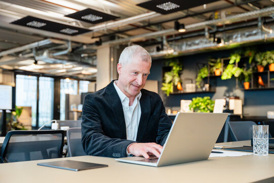 A smiling businessman types on a laptop in a modern office