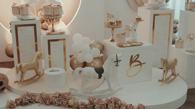 Christening dessert table with rocking horses cakes balloons roses and gold decor in a soft elegant setting