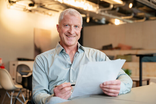 Smiling senior businessman holds a document in the modern office