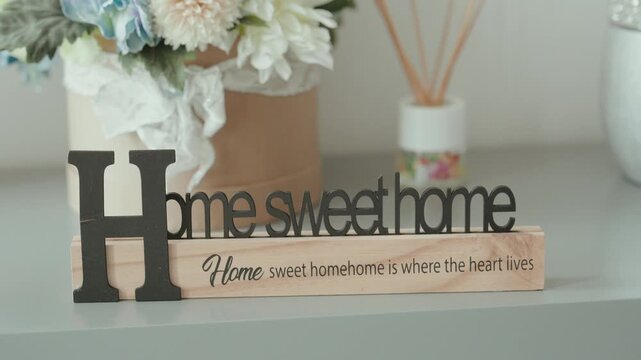 Home Sweet Home wooden decorative sign on a shelf beside flowers and a reed diffuser in a bright interior
