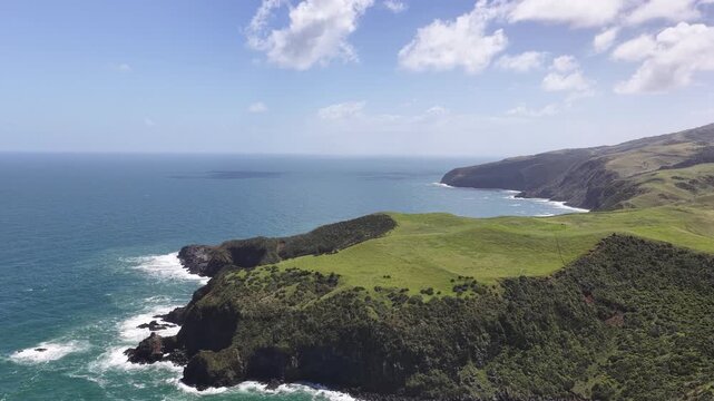 Aerial panorama of the rugged volcanic coastline on New Zealand's North Island, featuring dramatic sea cliffs, rolling green headlands, crashing Pacific waves and untouched coastal landscapes.