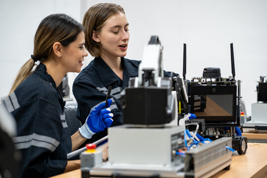 Collaborative Robotics Training: Two young female engineers work together, meticulously assembling a robotic arm, immersed in the practical application of advanced technology.