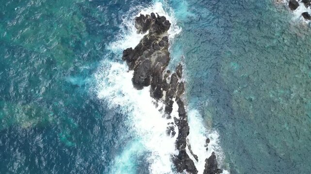 Aerial 4K top down drone view of white waves crashing on dark volcanic rocks in the clear blue Atlantic Ocean in Madeira, Portugal. Abstract natural seascape pattern from directly above.