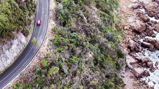 Red single car on Great Ocean road driving along the sea scenic aerial landscape.