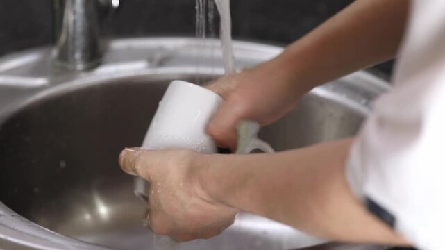Washing a white mug in the kitchen sink using a sponge and soapy water