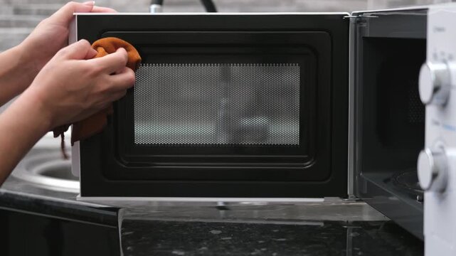 A woman's hand washes a white microwave oven in the kitchen
