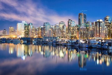 Fototapeta premium City skyline with tall buildings and boats on water at sunset