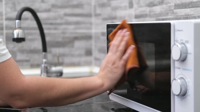 A woman's hand washes a white microwave oven in the kitchen
