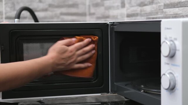 A woman's hand washes a white microwave oven in the kitchen