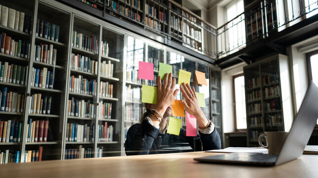 Woman brainstorming with colorful sticky notes in bright library.
