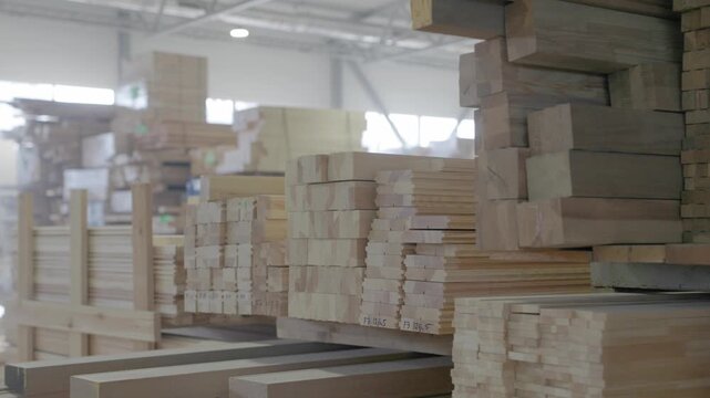 Stacked wooden profiles with marked measurements stored on factory shelving for window frame production