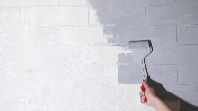 Close-up of a hand painting a white brick wall grey with a paint roller