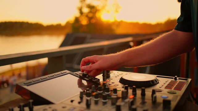 relaxed and focused outdoor sunset scene with a wooden deck and metal railing as a professional dj mixes music on a mixer in a side view setting, commercial and natural light background.
