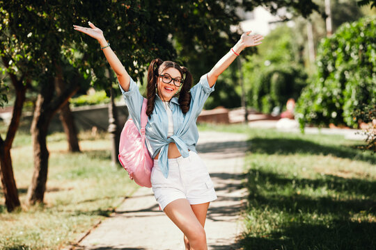 Young girl outdoors celebrating in park with backpack raised arms under sunny sky