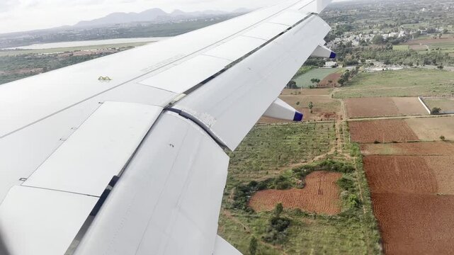 Full HD aerial footage from an airplane window showing the aircraft wing above patchwork farmland, rural roads and village buildings, capturing scenic flight travel and countryside landscape below.