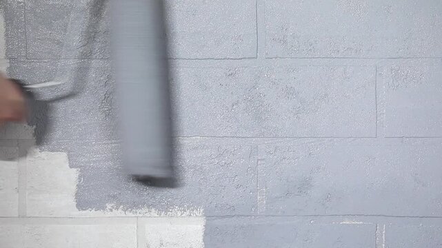 Close-up of a hand painting a white brick wall grey with a paint roller