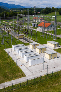 Aerial view shows battery energy storage system near power lines and buildings with green fields and mountains in the background.