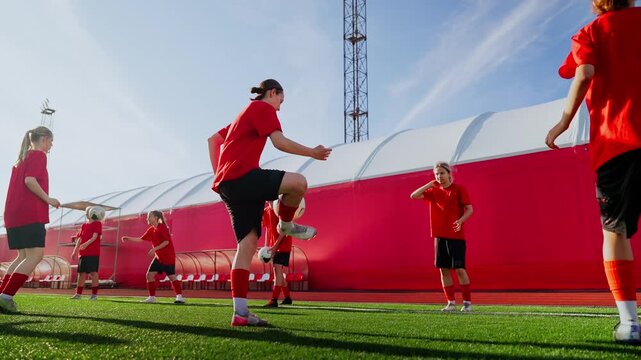 Womens soccer team practicing passing drills on green artificial turf field during daylight training session, developing coordination, ball control and teamwork skills
