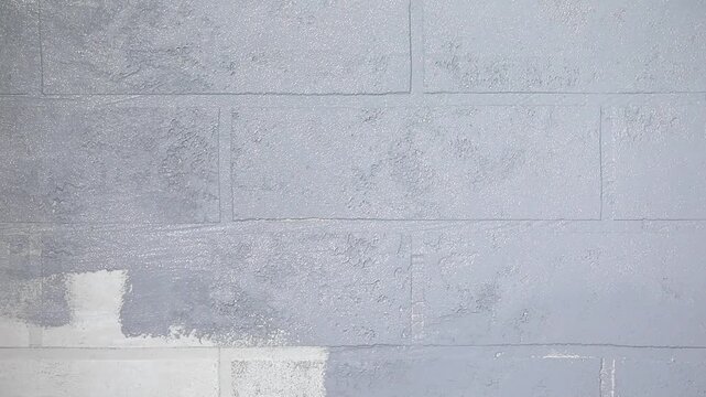 Close-up of a hand painting a white brick wall grey with a paint roller
