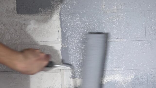 Close-up of a hand painting a white brick wall grey with a paint roller