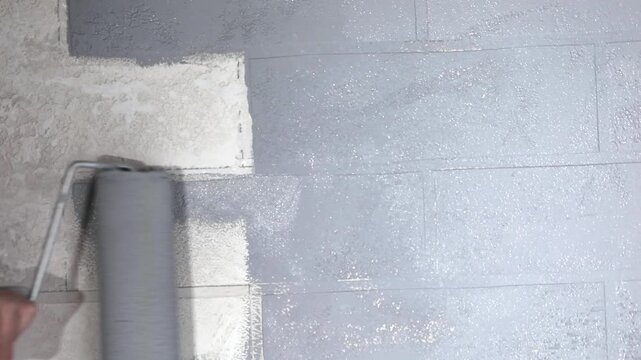 Close-up of a hand painting a white brick wall grey with a paint roller