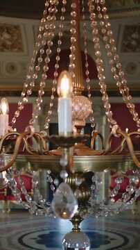 Vertical video: Camera moving inward toward brass crystal chandelier in grand hall, revealing bulbs
