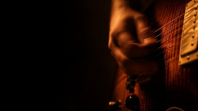 Man playing electric guitar in dark studio. Musician strumming strings on instrument with golden lighting. Performance, artistic skill and creative hobby. Sound and melody concept.