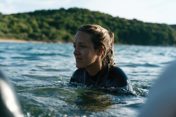 Fototapeta premium A thoughtful woman in a wetsuit reflects while sitting in tranquil waters surrounded by nature, demonstrating her passion for aquatic sports and love for the ocean.