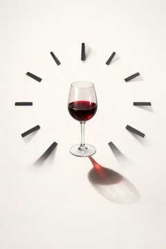 Glass of red wine placed in the center with black markers resembling clock numbers around it, creating a visual representation of time and enjoyment