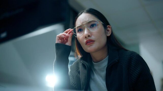 Female software developer wearing eyeglasses focuses on analyzing code at a computer during a night shift, representing software engineering, cybersecurity, AI, and modern information technology.