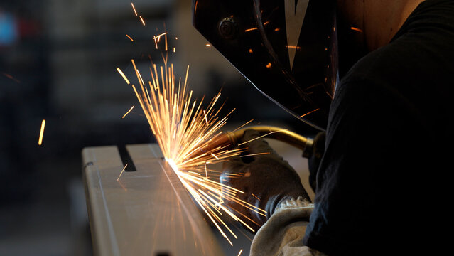Striking close-up of bright sparks flying from heavy industrial equipment during a metalworking process. The image captures the intense heat and dynamic energy of modern manufacturing