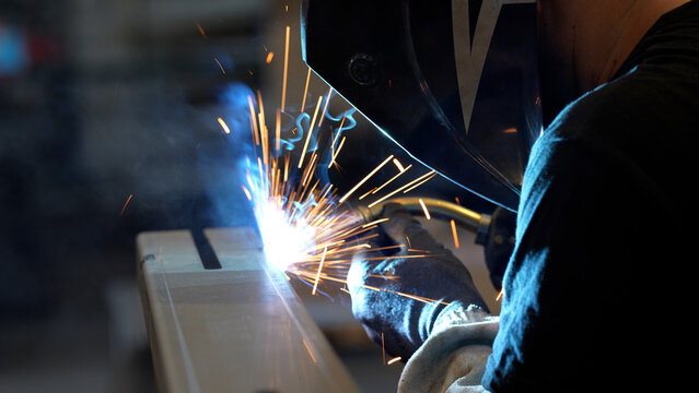 Striking close-up of bright sparks flying from heavy industrial equipment during a metalworking process. The image captures the intense heat and dynamic energy of modern manufacturing