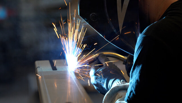Striking close-up of bright sparks flying from heavy industrial equipment during a metalworking process. The image captures the intense heat and dynamic energy of modern manufacturing
