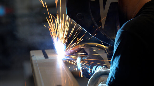 Striking close-up of bright sparks flying from heavy industrial equipment during a metalworking process. The image captures the intense heat and dynamic energy of modern manufacturing