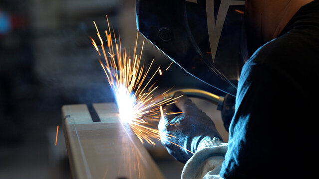 Striking close-up of bright sparks flying from heavy industrial equipment during a metalworking process. The image captures the intense heat and dynamic energy of modern manufacturing