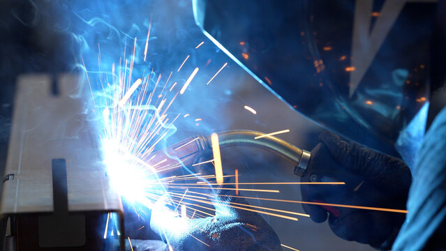 Striking close-up of bright sparks flying from heavy industrial equipment during a metalworking process. The image captures the intense heat and dynamic energy of modern manufacturing
